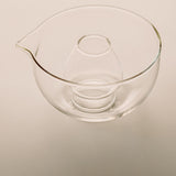Clear glass mixing bowl with a pouring spout and a smaller inner bowl, shown on a plain light beige background.