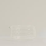A clear glass pitcher with a small pouring spout, photographed against a plain light gray studio background.